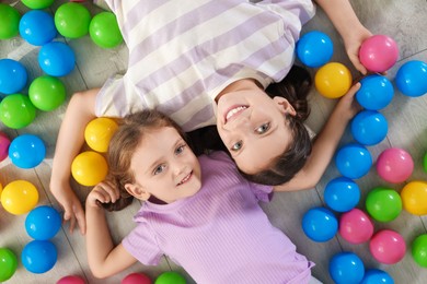 Photo of Cute little sisters playing with colorful balls on floor at home, top view