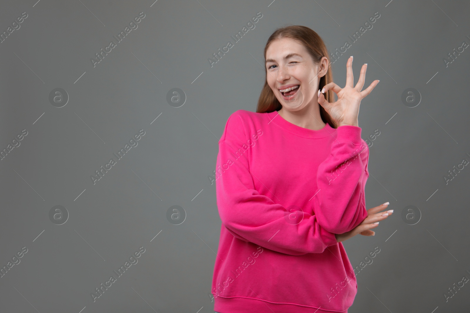 Photo of Smiling girl with braces showing ok gesture on grey background, space for text