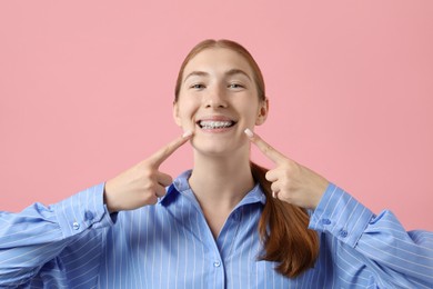 Photo of Girl pointing at her braces on pink background