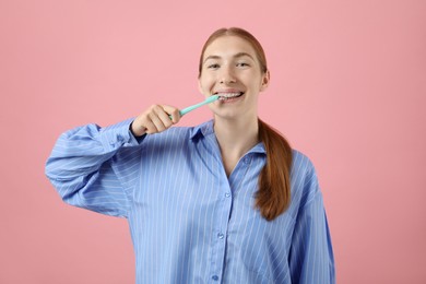 Photo of Girl with braces cleaning teeth on pink background