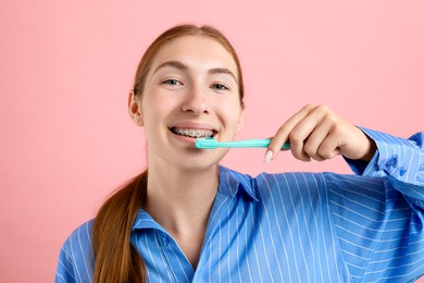 Photo of Girl with braces cleaning teeth on pink background