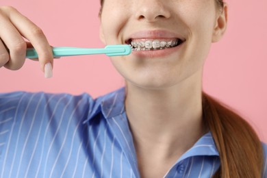 Photo of Girl with braces cleaning teeth on pink background, closeup