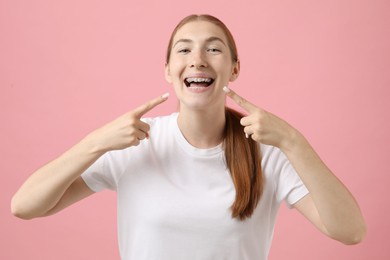 Photo of Girl pointing at her braces on pink background