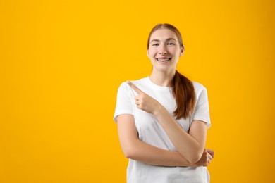 Photo of Smiling girl with braces on orange background, space for text