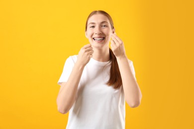 Photo of Girl with braces cleaning teeth with dental floss on orange background