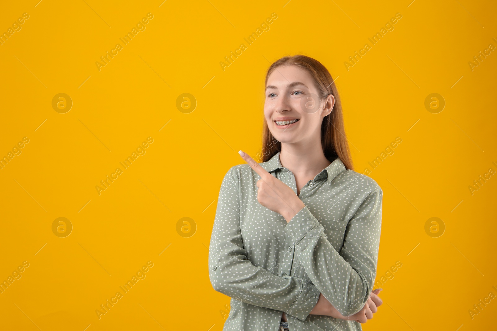 Photo of Smiling girl with braces on orange background, space for text