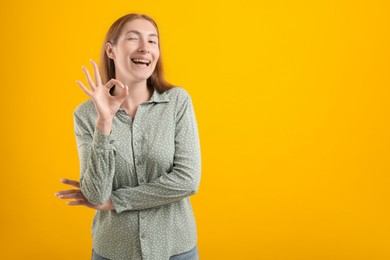 Photo of Smiling girl with braces showing ok gesture on orange background, space for text