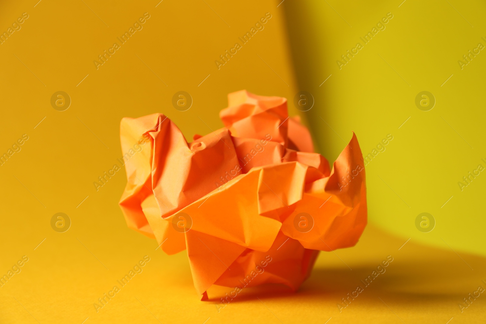 Photo of Orange crumpled paper on yellow background, closeup