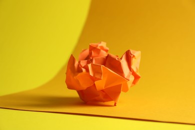 Photo of Orange crumpled paper on yellow background, closeup