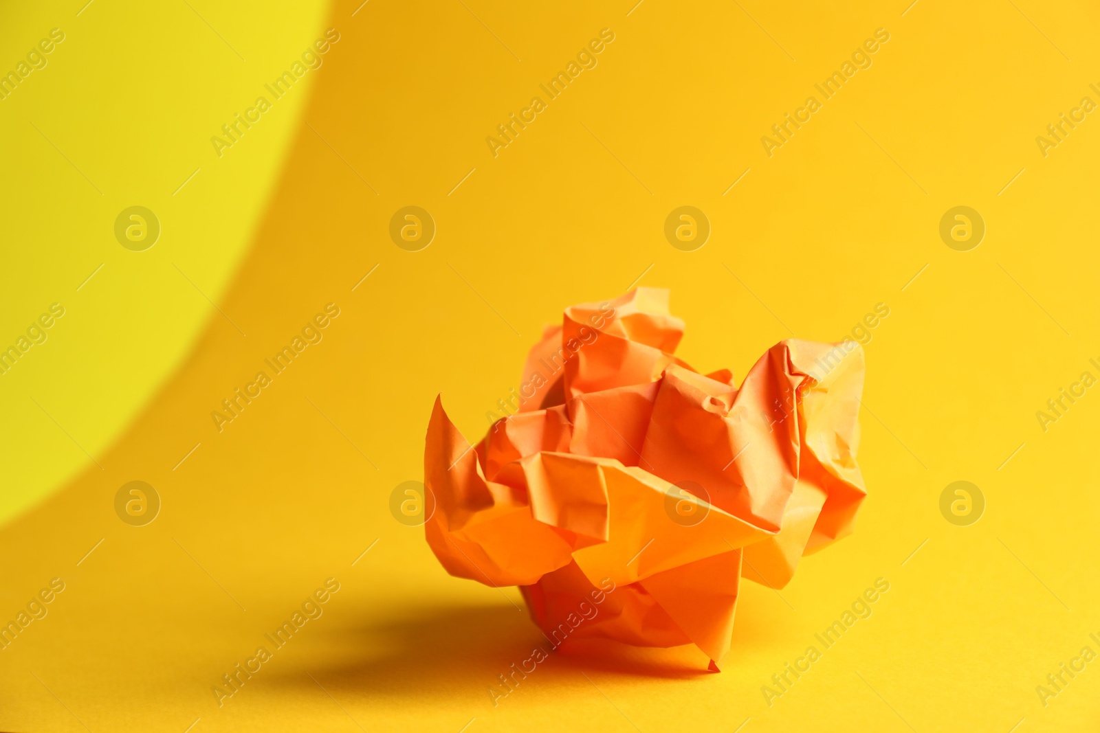 Photo of Orange crumpled paper on yellow background, closeup