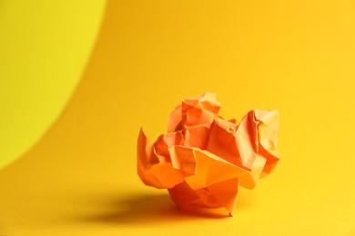 Photo of Orange crumpled paper on yellow background, closeup