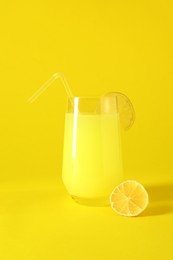 Fresh juice in glass and lemon on yellow background