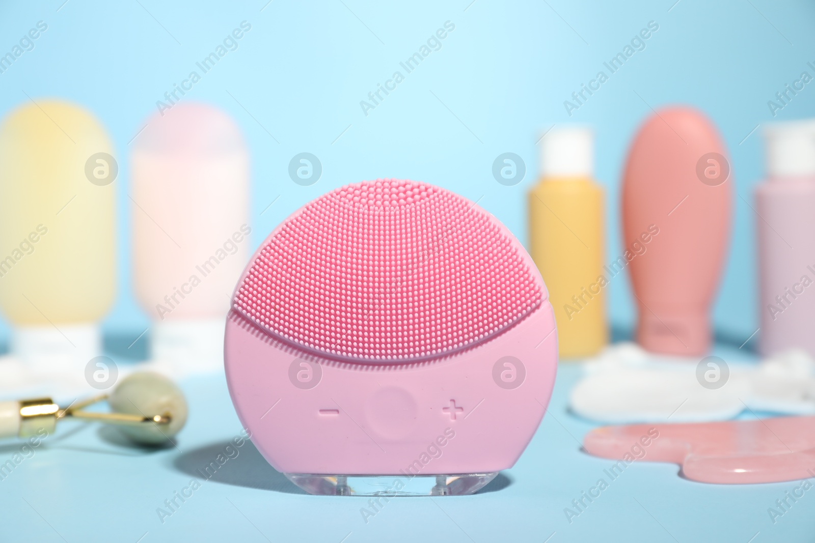 Photo of Facial cleansing brush and other skin care products on light blue background