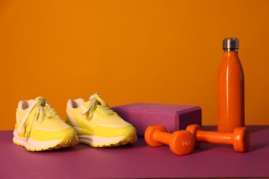 Photo of Stylish sneakers, thermo bottle, dumbbells and yoga block on color background