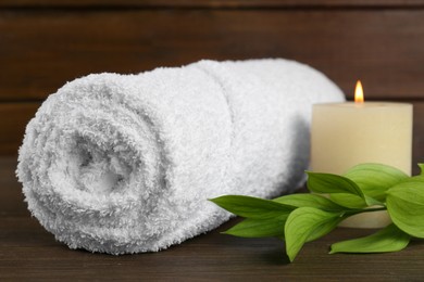 Photo of Spa composition. Towel, burning candle and green leaves on wooden table, closeup