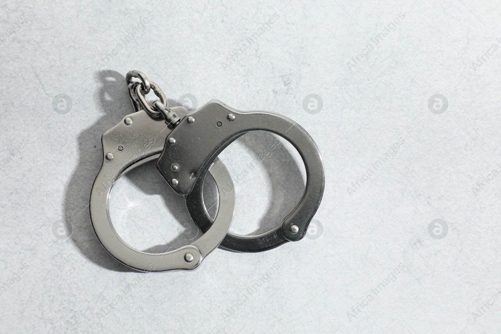 Photo of Metal chain handcuffs on light grey table, top view. Space for text