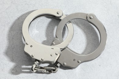 Metal chain handcuffs on light grey table, closeup