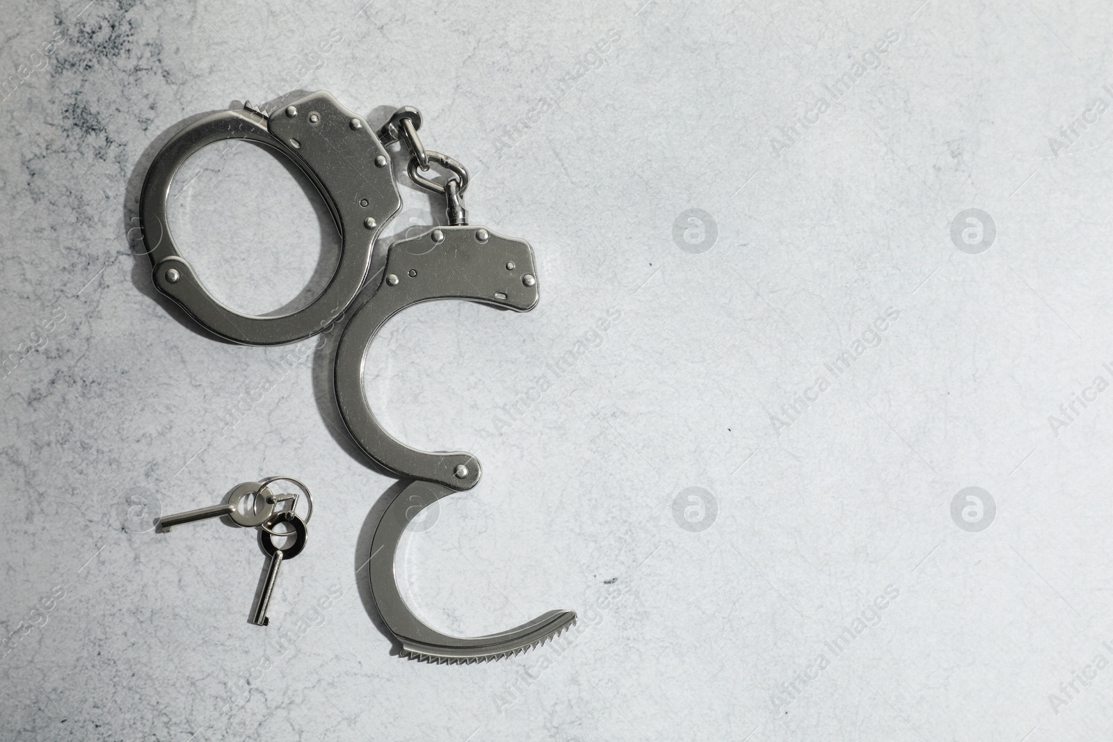 Photo of Metal chain handcuffs and keys on light grey table, top view. Space for text