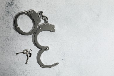 Photo of Metal chain handcuffs and keys on light grey table, top view. Space for text