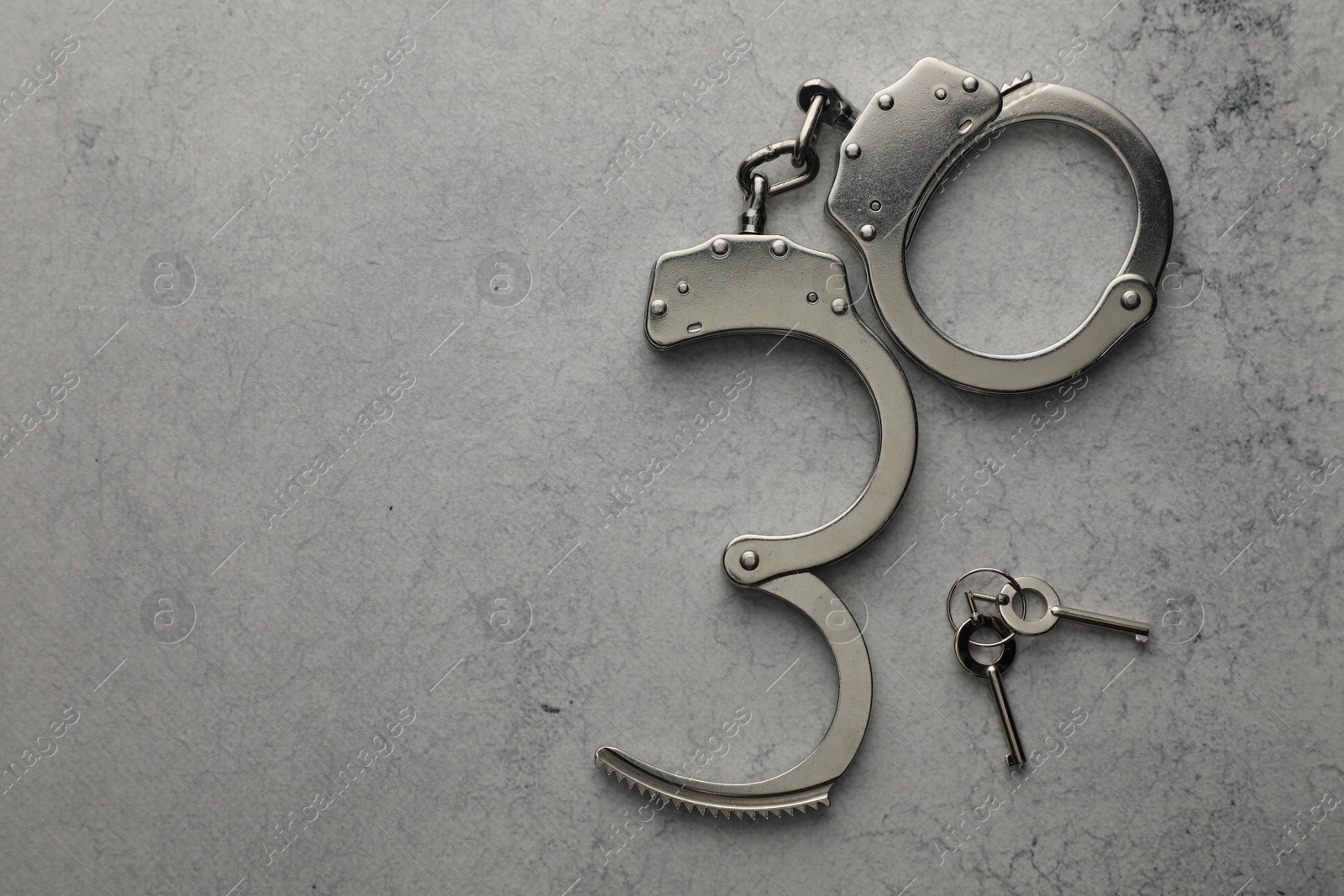 Photo of Metal chain handcuffs and keys on light grey table, top view. Space for text