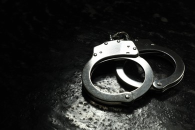 Photo of Metal chain handcuffs on black table, closeup. Space for text