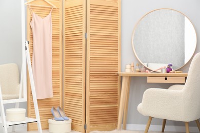 Mirrors, dressing table with cosmetic products, armchair and folding screen indoors. Interior design