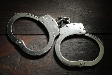 Metal chain handcuffs on wooden table, top view