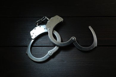 Photo of Metal chain handcuffs on black wooden table, top view