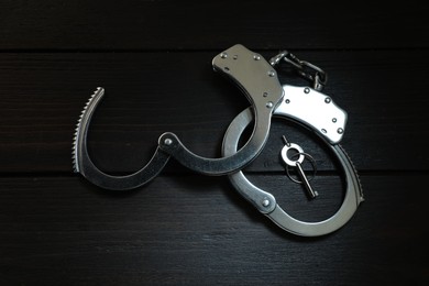 Photo of Metal chain handcuffs and key on black wooden table, top view