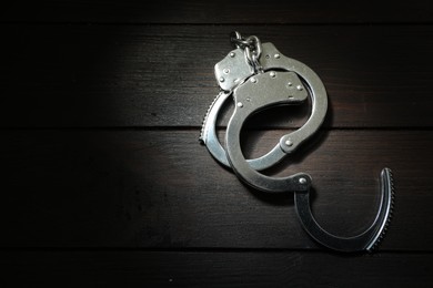 Metal chain handcuffs on black wooden table, top view. Space for text