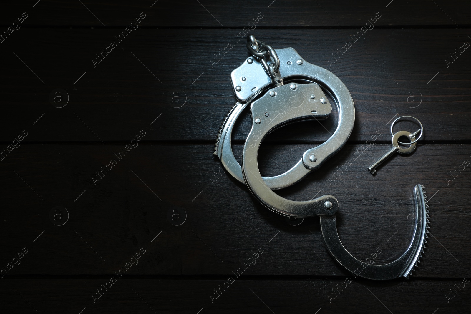 Photo of Metal chain handcuffs and key on black wooden table, top view. Space for text