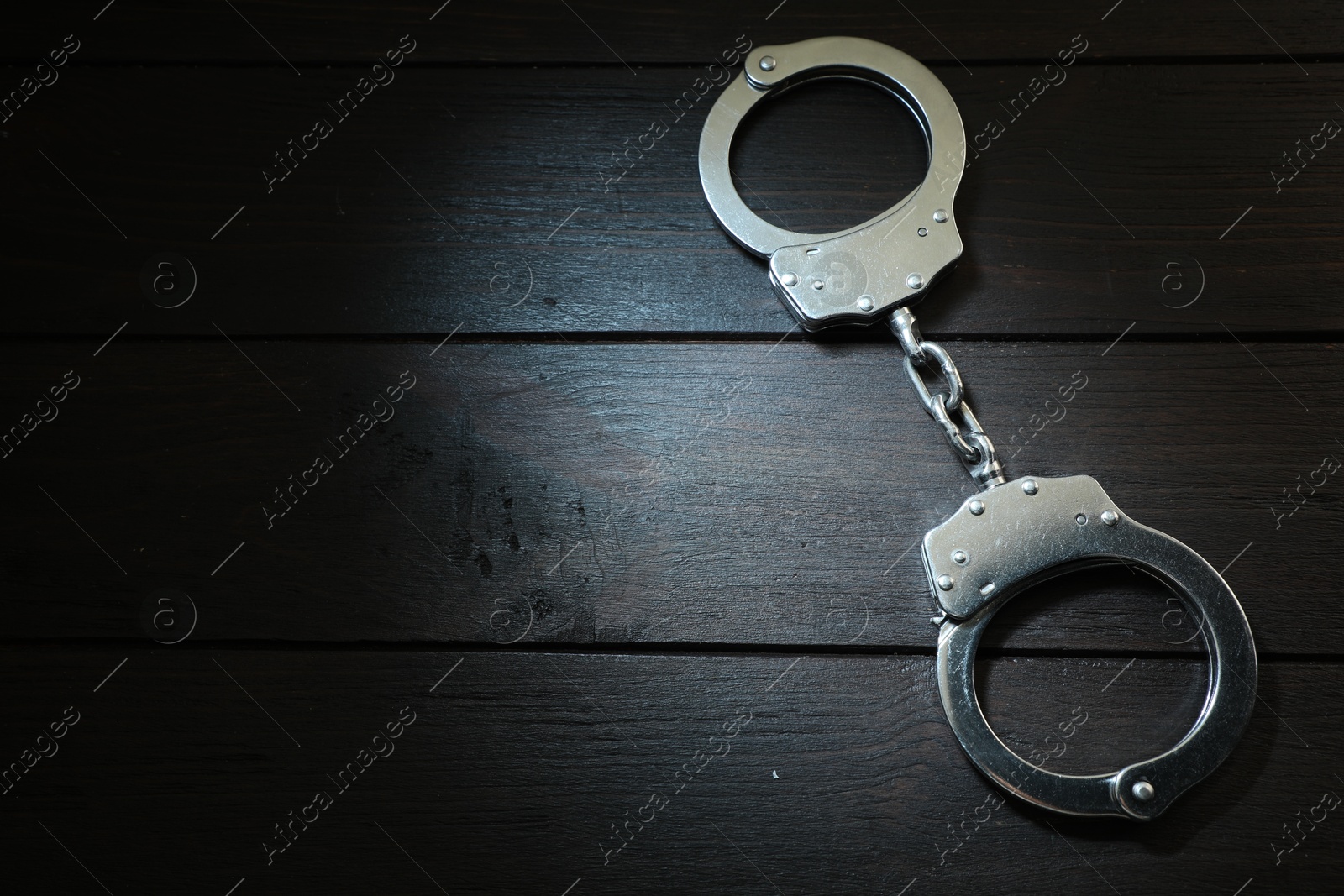 Photo of Metal chain handcuffs on black wooden table, top view. Space for text