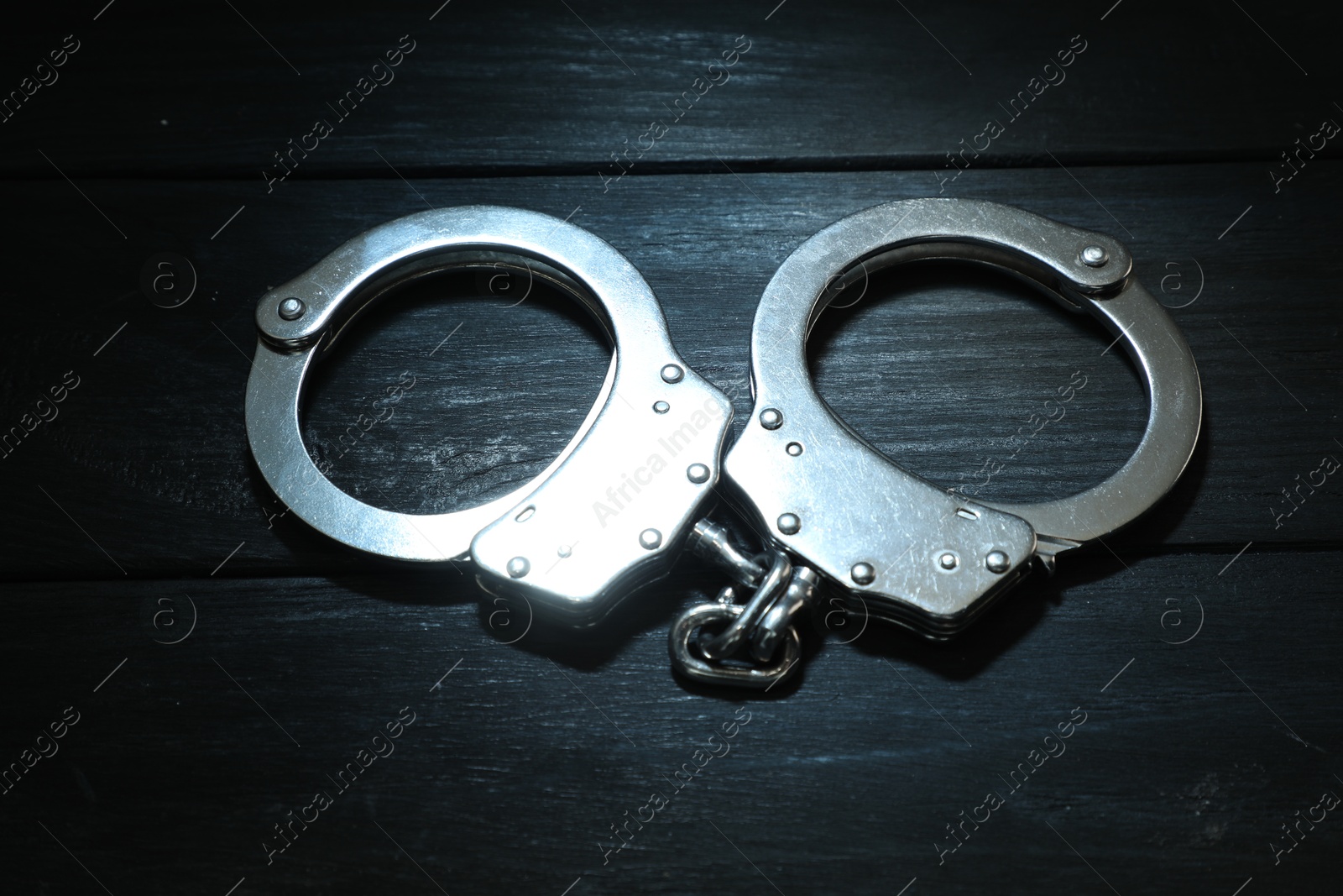 Photo of Metal chain handcuffs on black wooden table, closeup