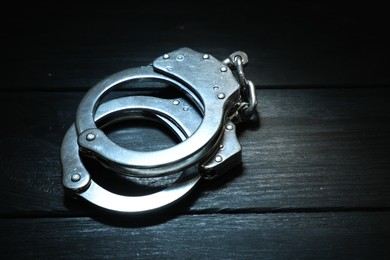 Photo of Metal chain handcuffs on black wooden table, closeup