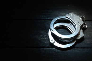 Photo of Metal chain handcuffs on black wooden table, closeup. Space for text