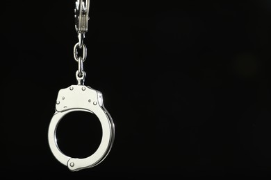 Photo of Metal chain handcuffs on black background, closeup. Space for text