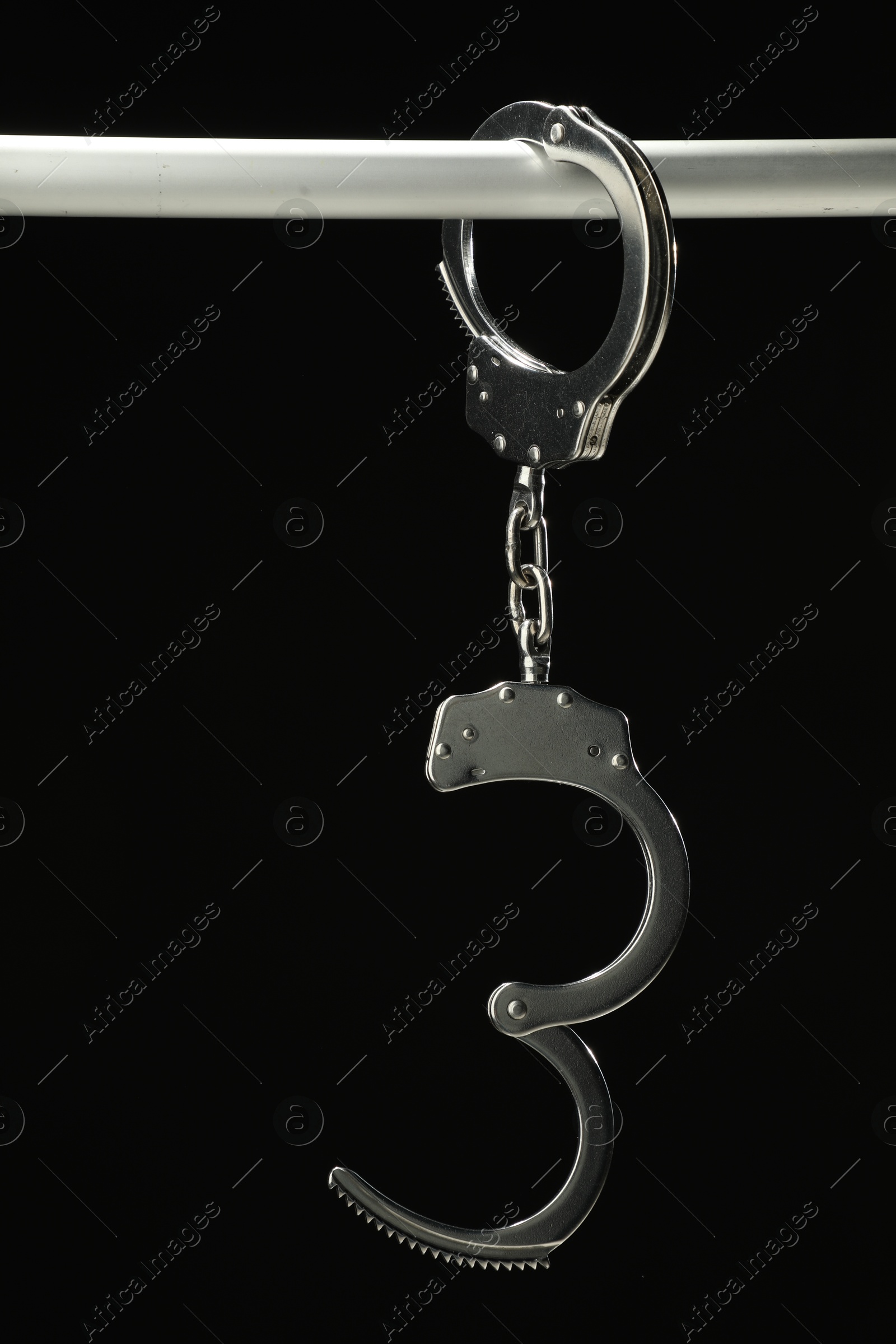 Photo of Metal chain handcuffs on pipe against black background, closeup