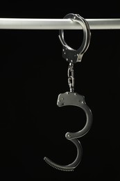 Photo of Metal chain handcuffs on pipe against black background, closeup