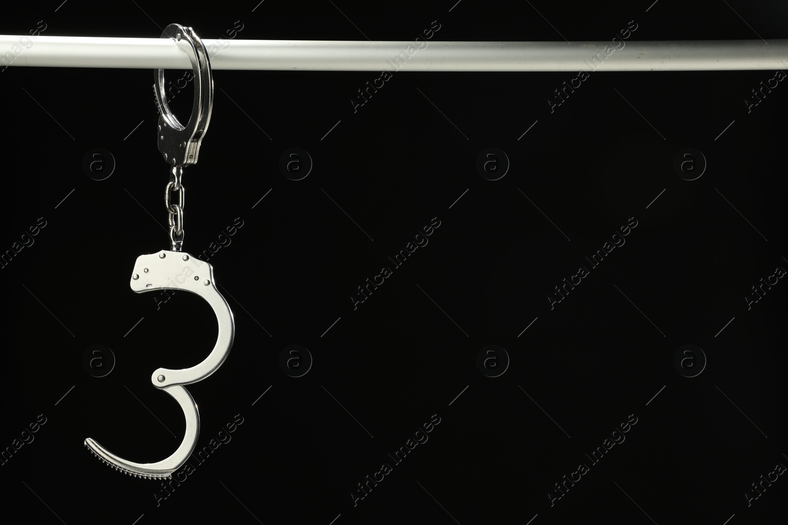 Photo of Metal chain handcuffs on pipe against black background, closeup. Space for text