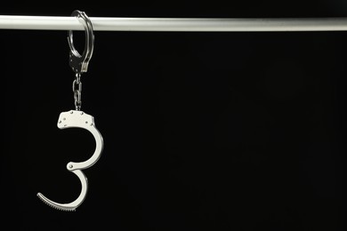 Photo of Metal chain handcuffs on pipe against black background, closeup. Space for text