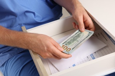 Photo of Corruption concept. Doctor putting dollar banknotes into drawer, closeup