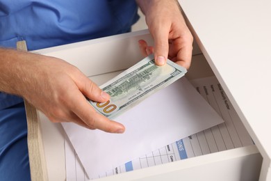 Photo of Corruption concept. Doctor putting dollar banknotes into drawer, closeup