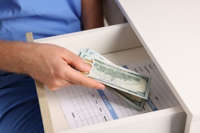 Photo of Corruption concept. Doctor putting dollar banknotes into drawer, closeup