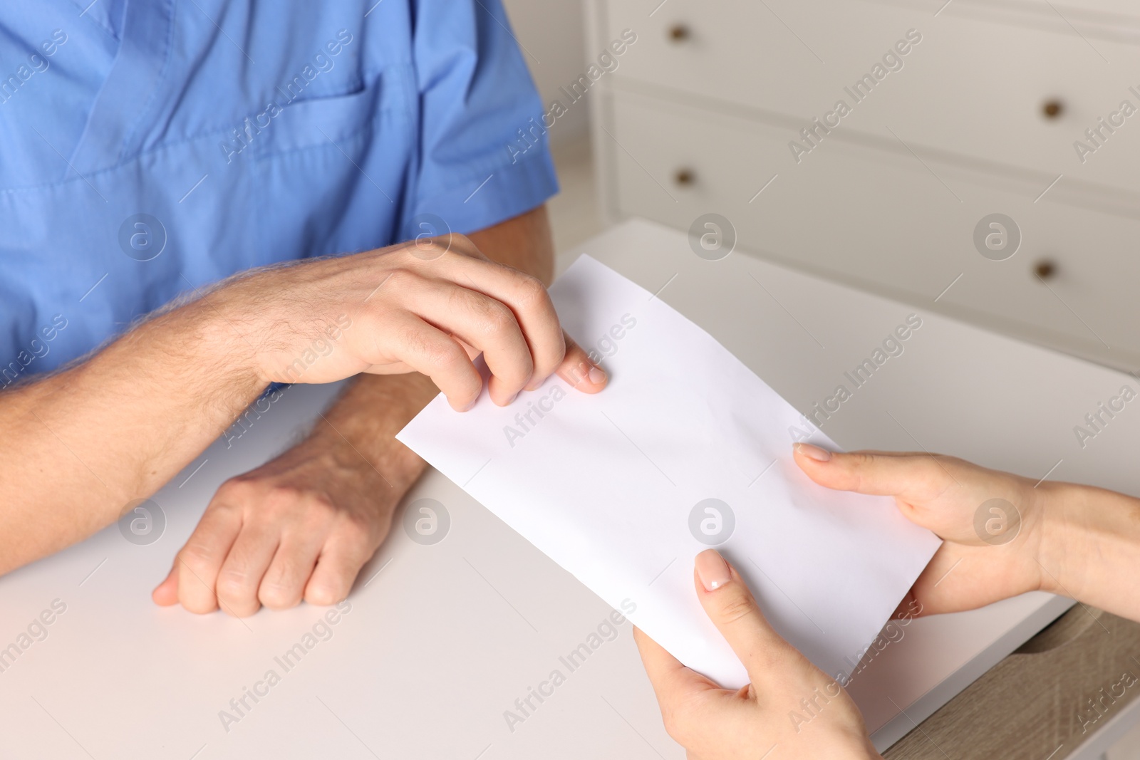 Photo of Corruption concept. Woman giving envelope with money to doctor at white table, closeup