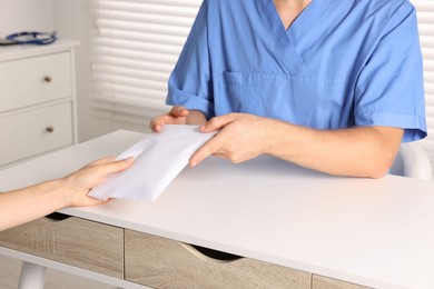 Photo of Corruption concept. Woman giving envelope with money to doctor at white table, closeup