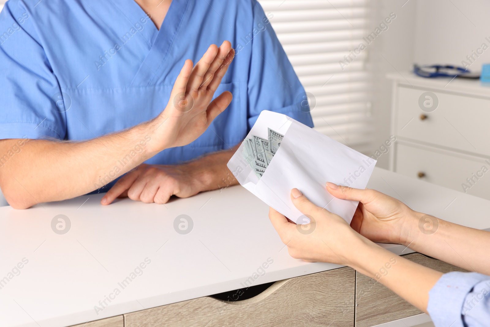 Photo of Corruption concept. Woman giving envelope with dollar banknotes to doctor at white table, closeup