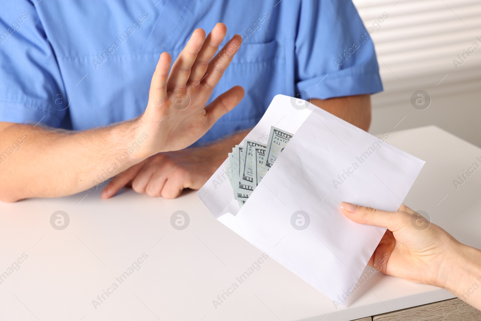 Photo of Corruption concept. Woman giving envelope with dollar banknotes to doctor at white table, closeup