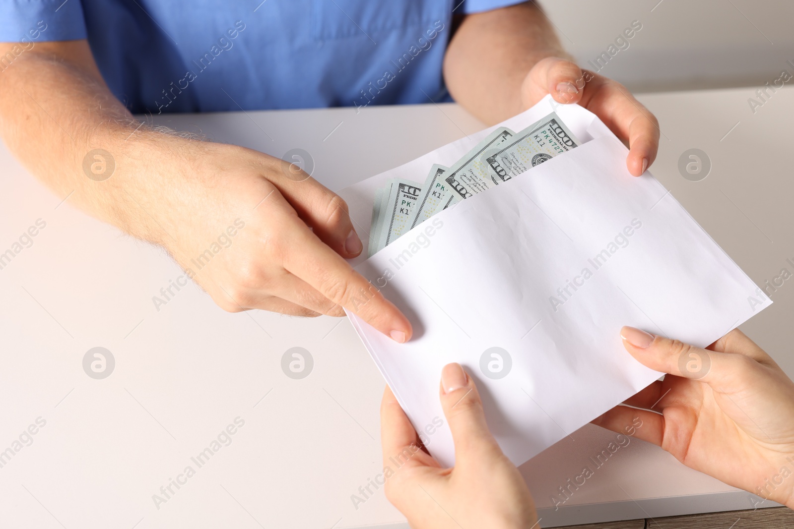 Photo of Corruption concept. Woman giving envelope with dollar banknotes to doctor at white table, closeup