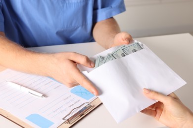 Photo of Corruption concept. Woman giving envelope with dollar banknotes to doctor at white table, closeup