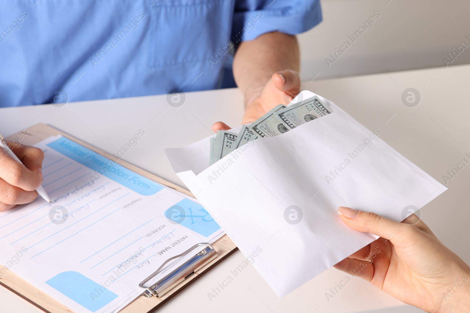 Photo of Corruption concept. Woman giving envelope with dollar banknotes to doctor at white table, closeup